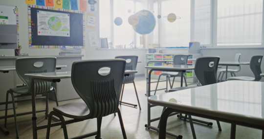 Empty elementary school classroom with desks and bright window light.