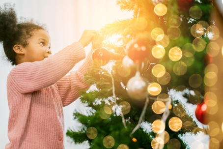 A cute little girl decorates a Christmas tree with ornaments.