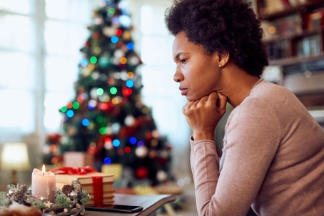 A lonely woman sitting in front of Christmas tree looking sad.