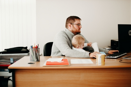 father with small child at a desk doing work on computer