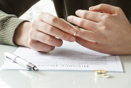 person taking off wedding ring over divorce papers