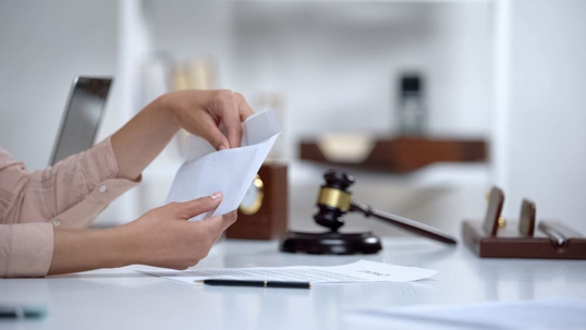 Woman reaching into envelope with gavel in the background