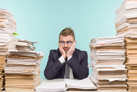A professional surrounded by large stacks of paperwork, representing the challenge of managing long-standing records and background information.